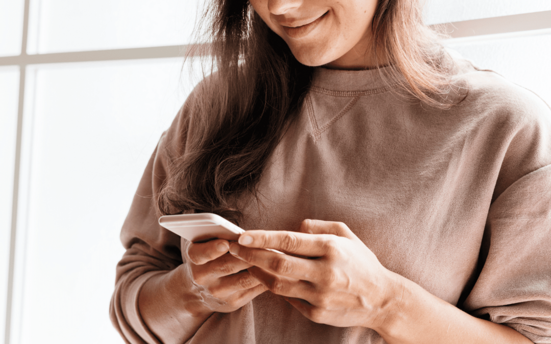 Smiling woman standing and holding her mobile phone on both hands